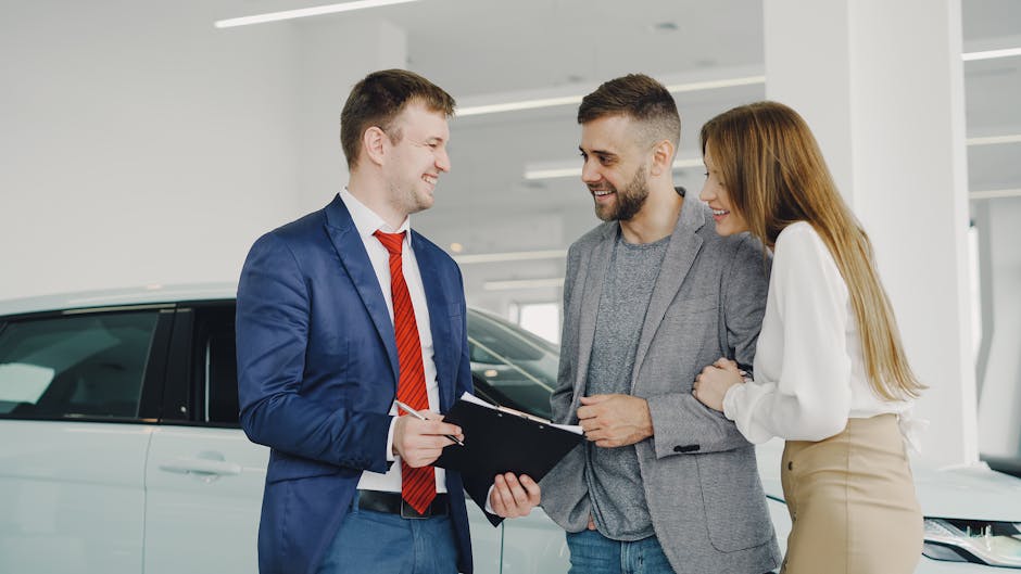 A smiling couple buys a new car from a confident salesman inside a modern car dealership.