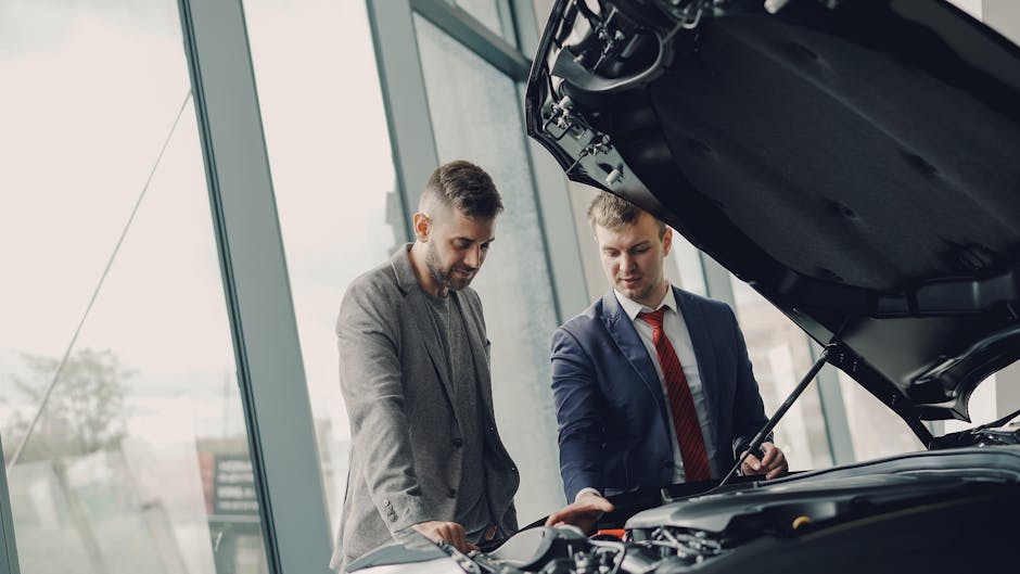 Two men inspecting a car's engine hood in a dealership showroom
